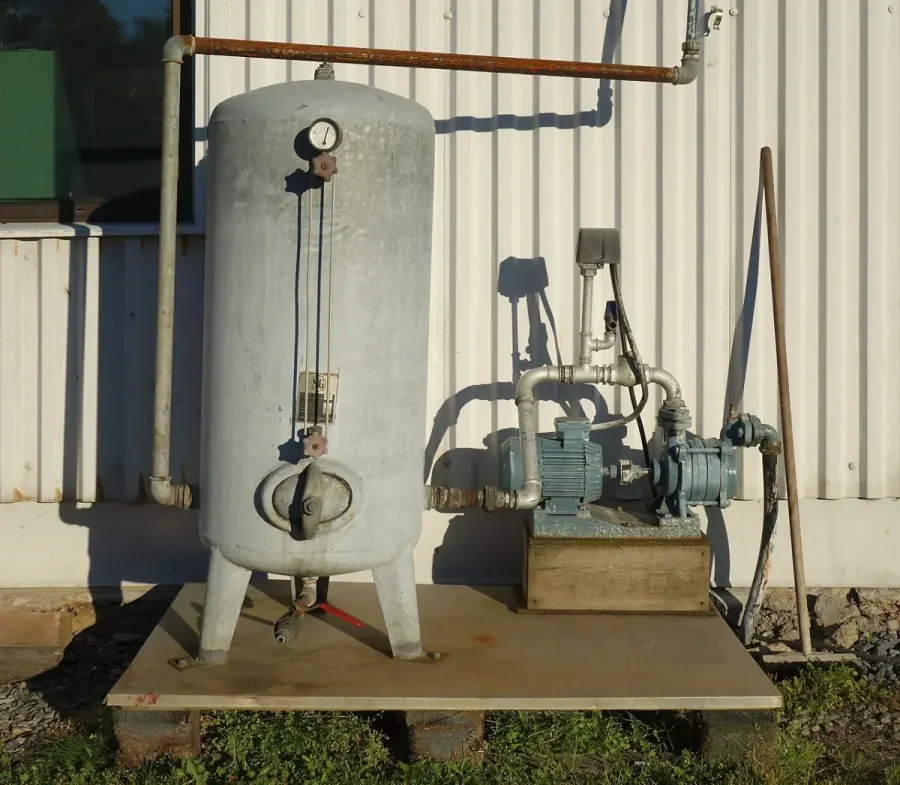 Galvanized pressure tank and pump set on a concrete pad outside a building in El Paso TX