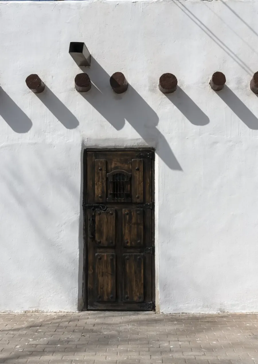 Whitewashed adobe wall with exposed vigas and a heavy wooden door in San Elizario TX, El Paso County